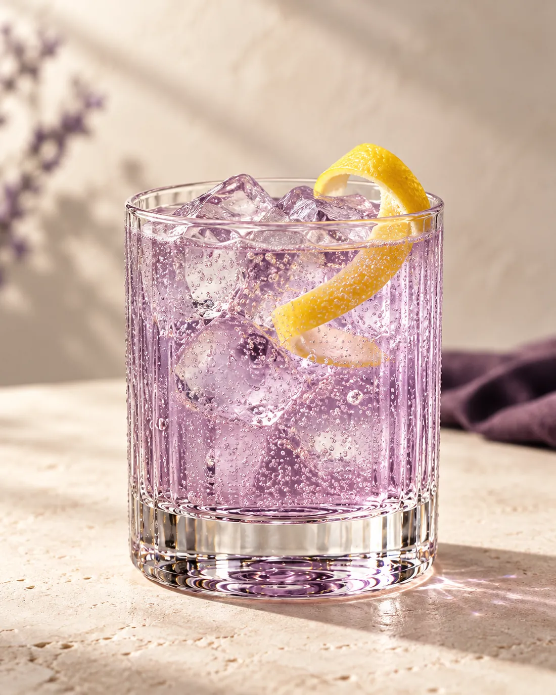 Purple gin and tonic with ice and lemon zest in a ribbed tumbler